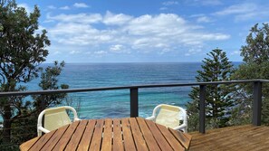 Eine Holzterrasse mit zwei weißen Stühlen mit Blick auf das klare, blaue Meer.