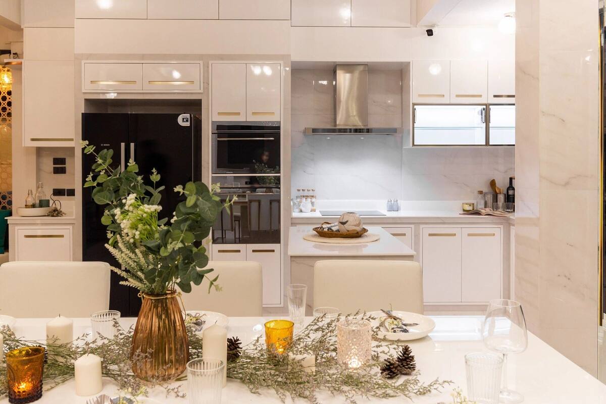 A modern kitchen with white cabinetry, a built-in oven, and a dining area set with a table, candles, and a vase of greenery.