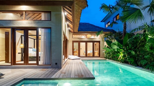 Een modern resort met een zwembad, houten terras en weelderige tropische planten.