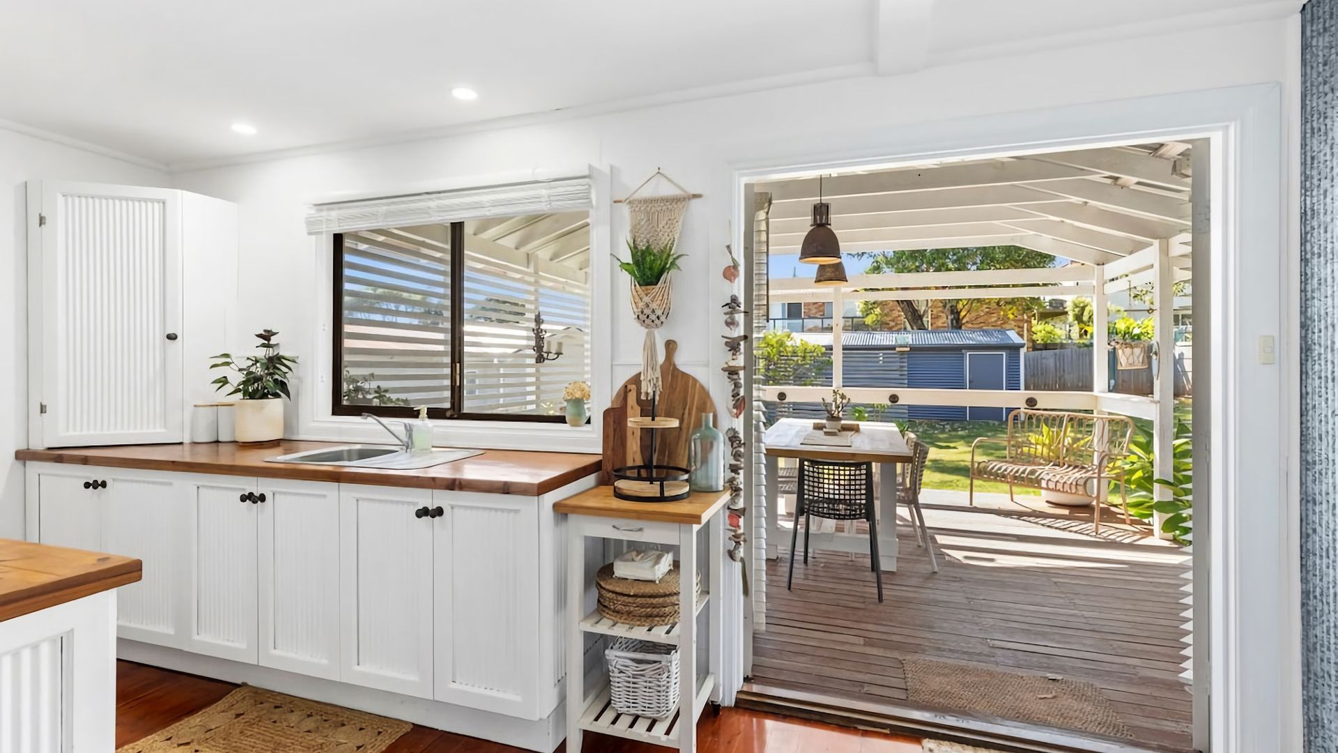 A modern kitchen with white cabinetry, a wooden countertop, and a view to a covered outdoor area with a table and chairs.
