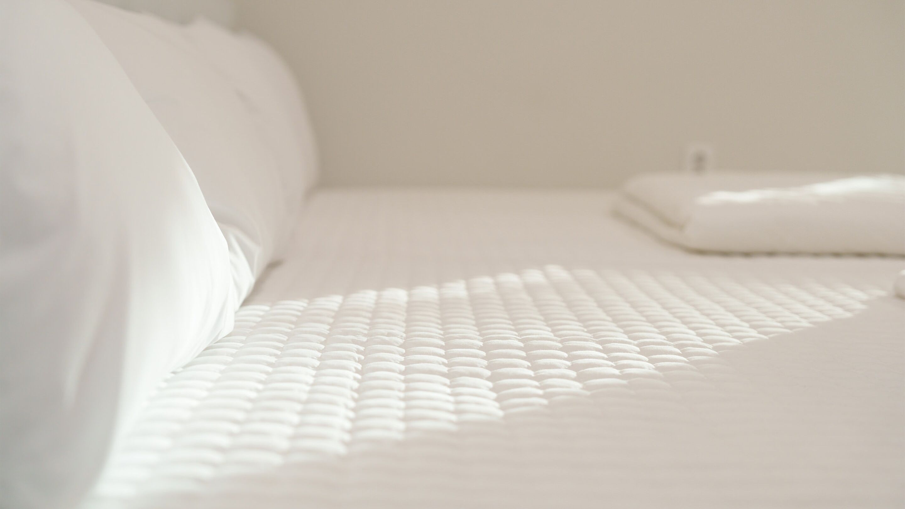 A neatly made bed with a white duvet and pillows, a white blanket, and a folded white towel on the side.