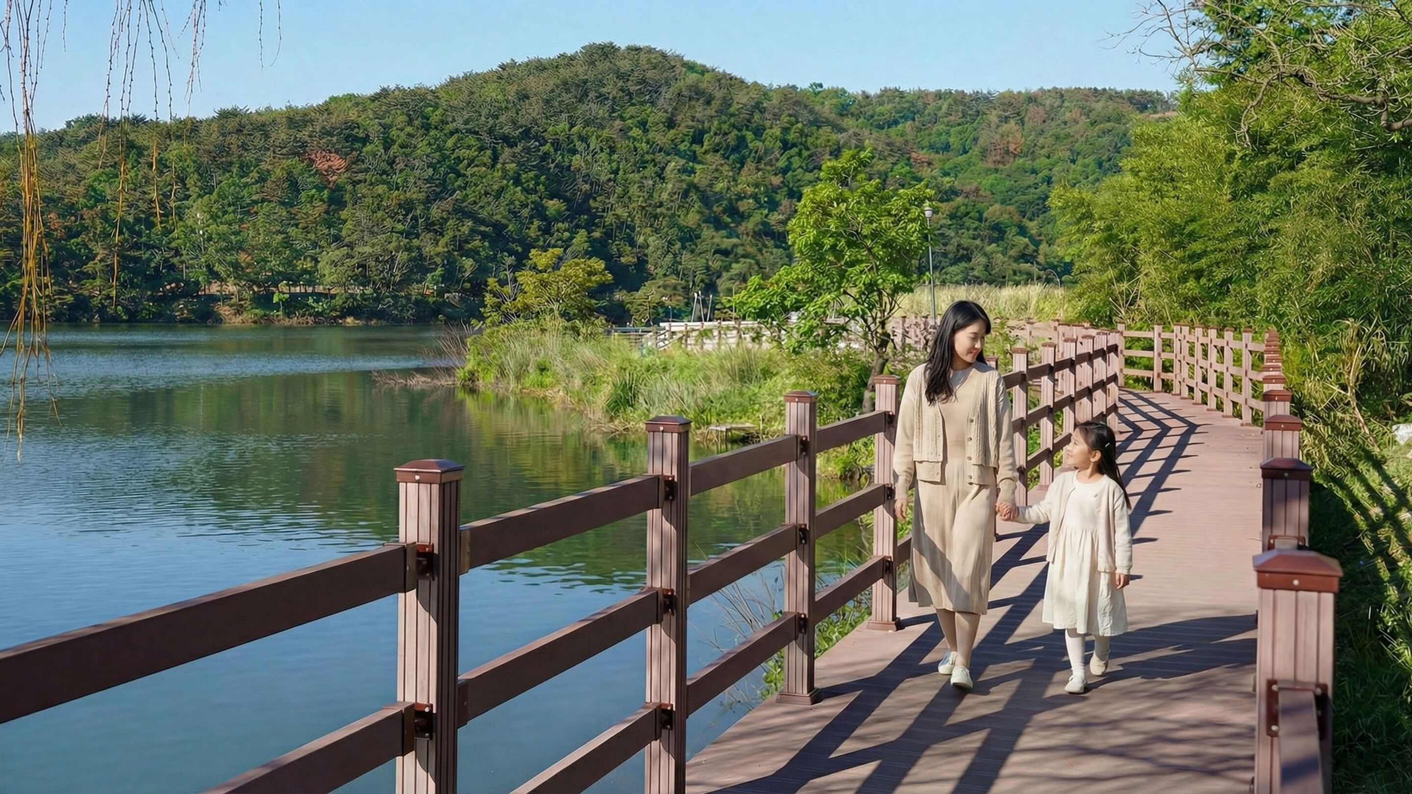 A wooden bridge over a calm lake with dense greenery in the background.
