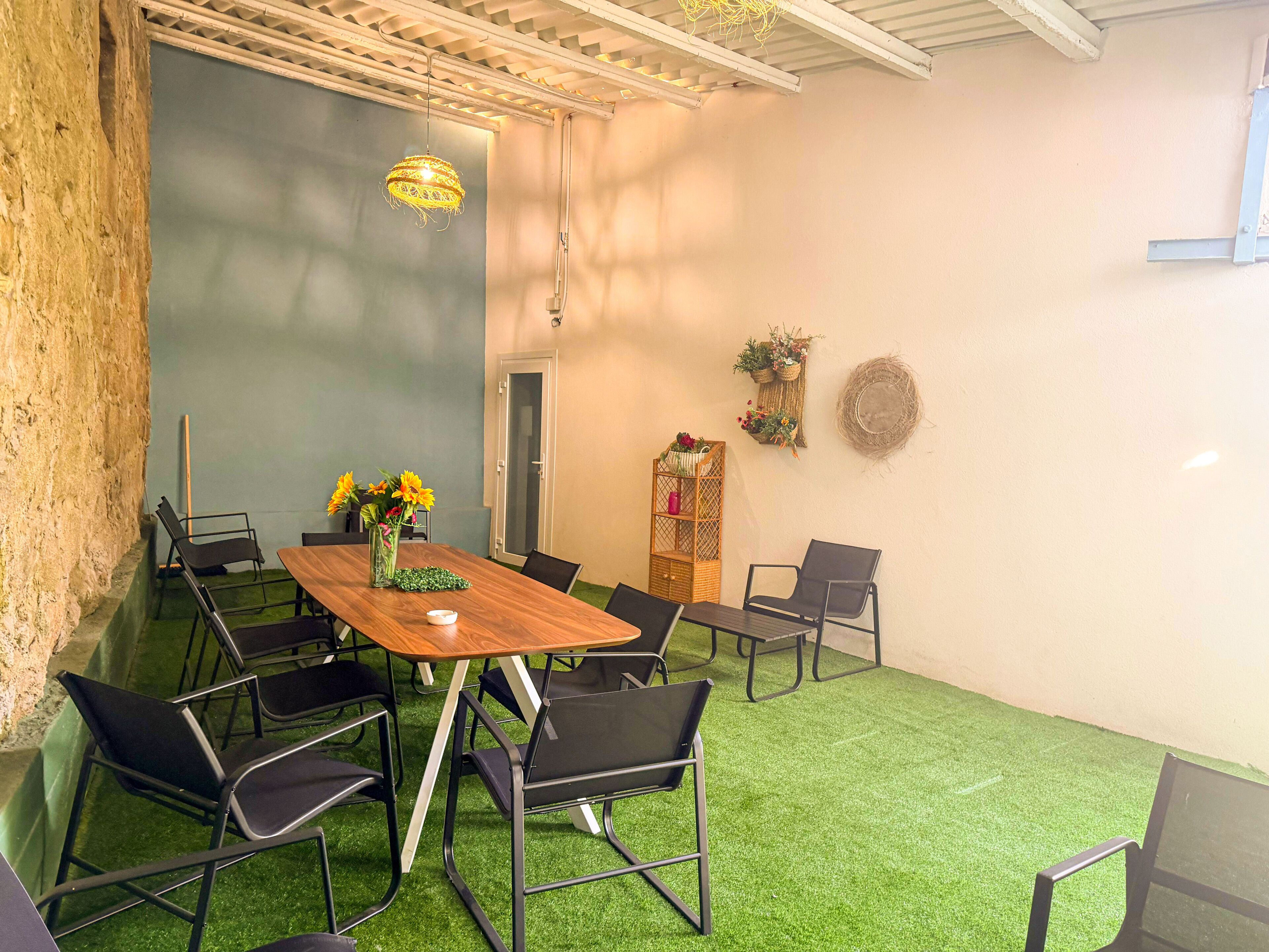 Un salón de conferencias con una mesa de madera, sillas negras, un florero, una lámpara colgante y un piso de césped artificial verde.