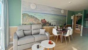 A living room with a sofa, two small round tables, and a dining area with chairs. - Luxury Singular Apartments Padrón (Padron)