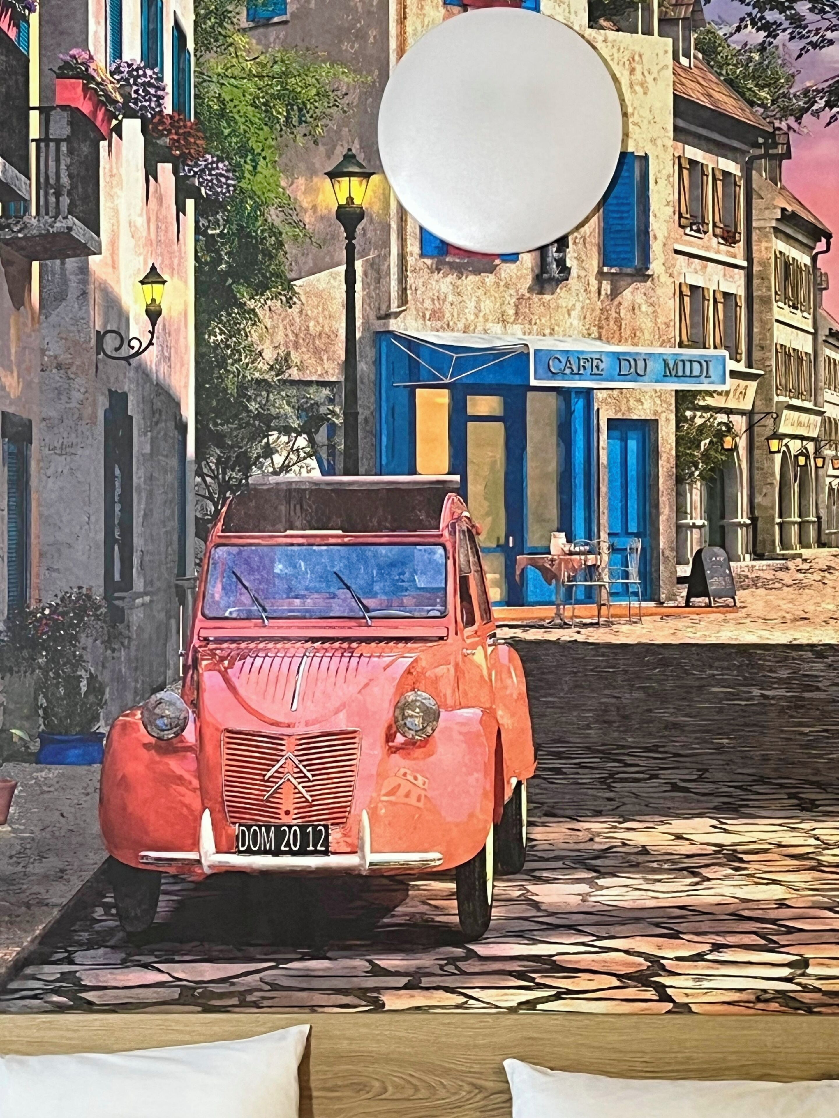 A vintage red car parked in front of a building with a blue sign reading 'CAFE DU MIDI'.