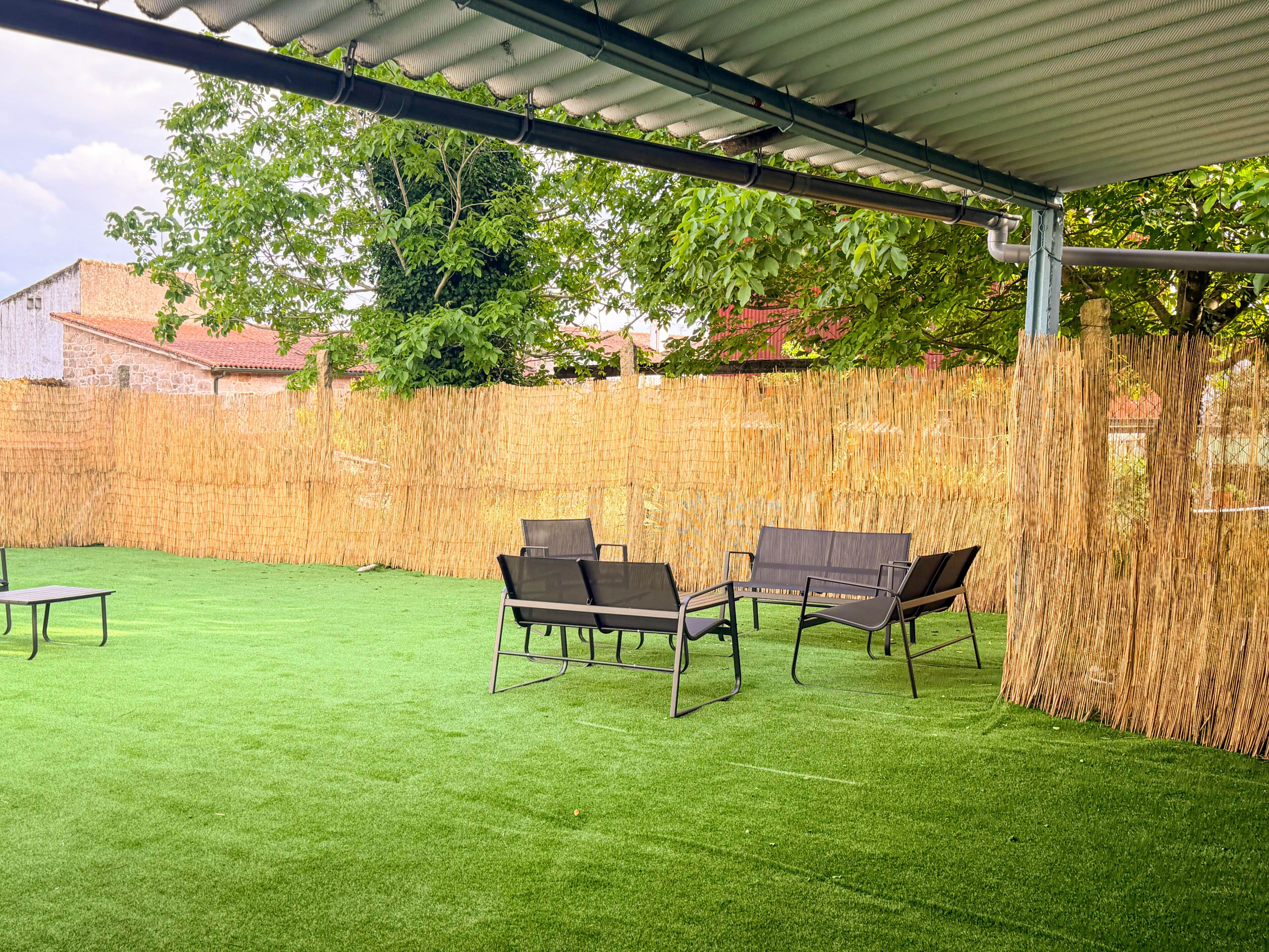 A covered patio area with artificial grass, outdoor furniture, and a bamboo fence.