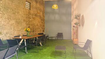 A room with a rustic stone wall, a wooden table with chairs, a small stool, and a hanging light fixture.