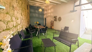 A room with a wooden table, black chairs, a green artificial turf floor, a stone wall, and a hanging light fixture. - Luxury Singular Apartments Padrón (Padron)