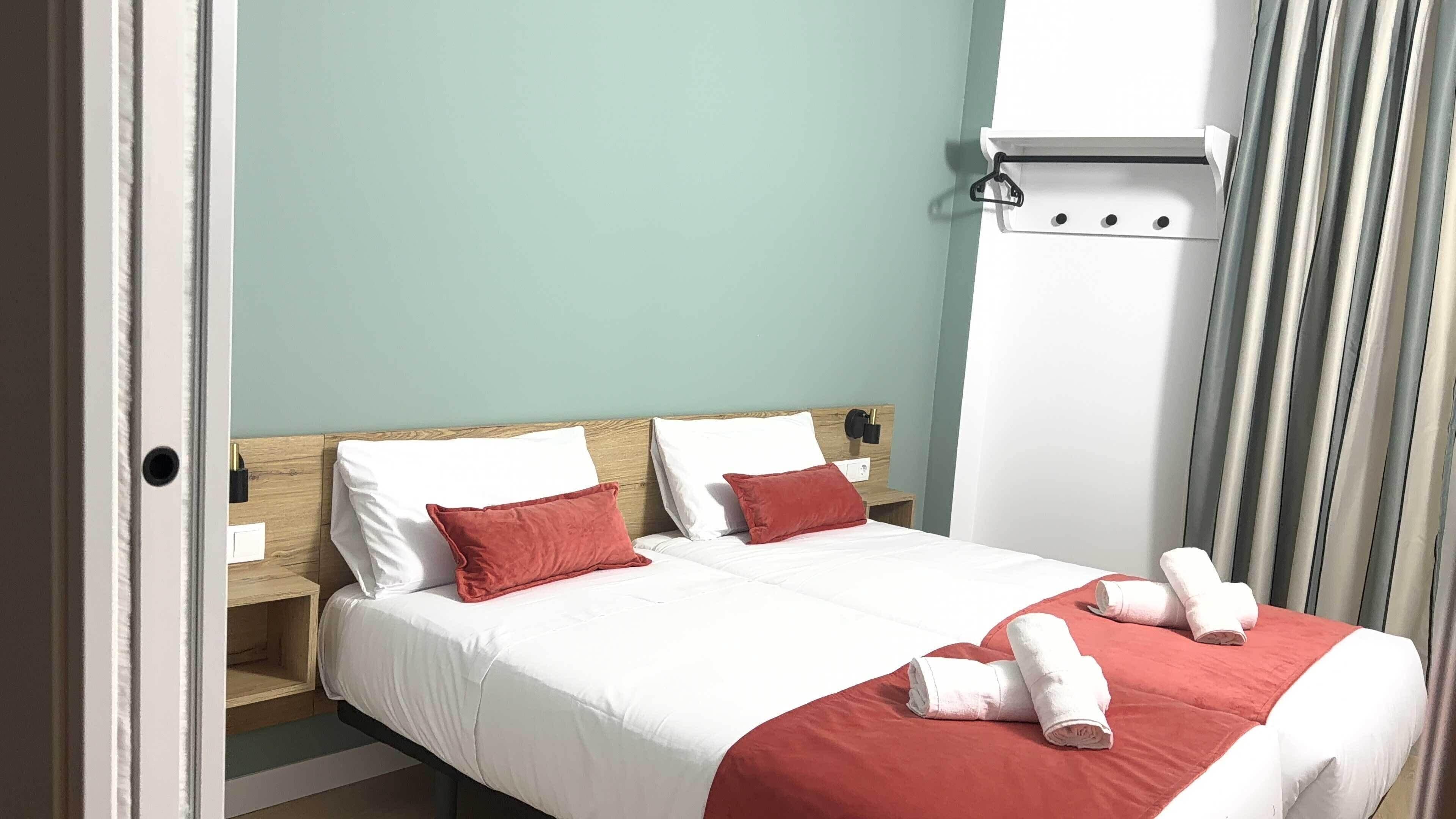 Cama bem arrumada com roupa de cama branca e vermelha, cabeceira de madeira e mesa de cabeceira branca.
