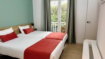 Habitación de hotel con cama doble, mesita de noche, ventana con cortinas y vista a zonas verdes.