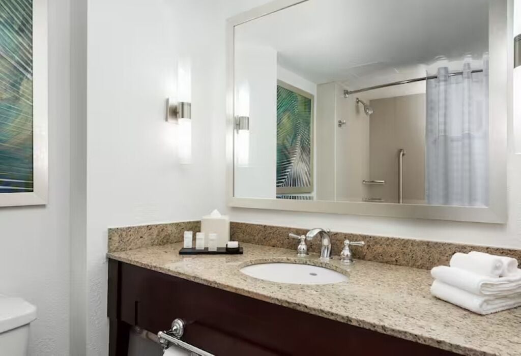 Un baño moderno con encimera de granito, un lavabo blanco y un espejo grande.