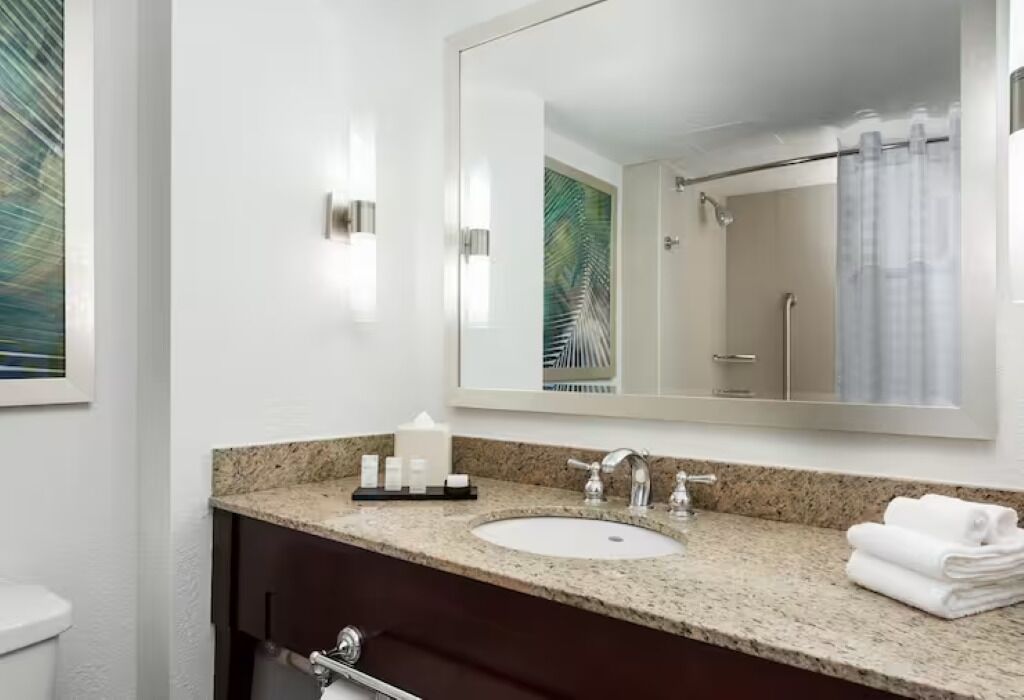 Un baño moderno con encimera de granito, un lavabo blanco y un espejo grande.