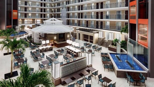 Un atrium d’hôtel à plusieurs niveaux, comprenant un bar central, un espace repas et une piscine.