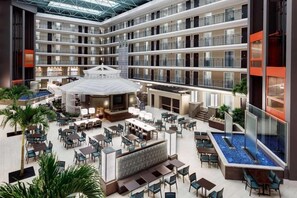 Um átrio de hotel com vários níveis, com um bar central, área de refeições e piscina.