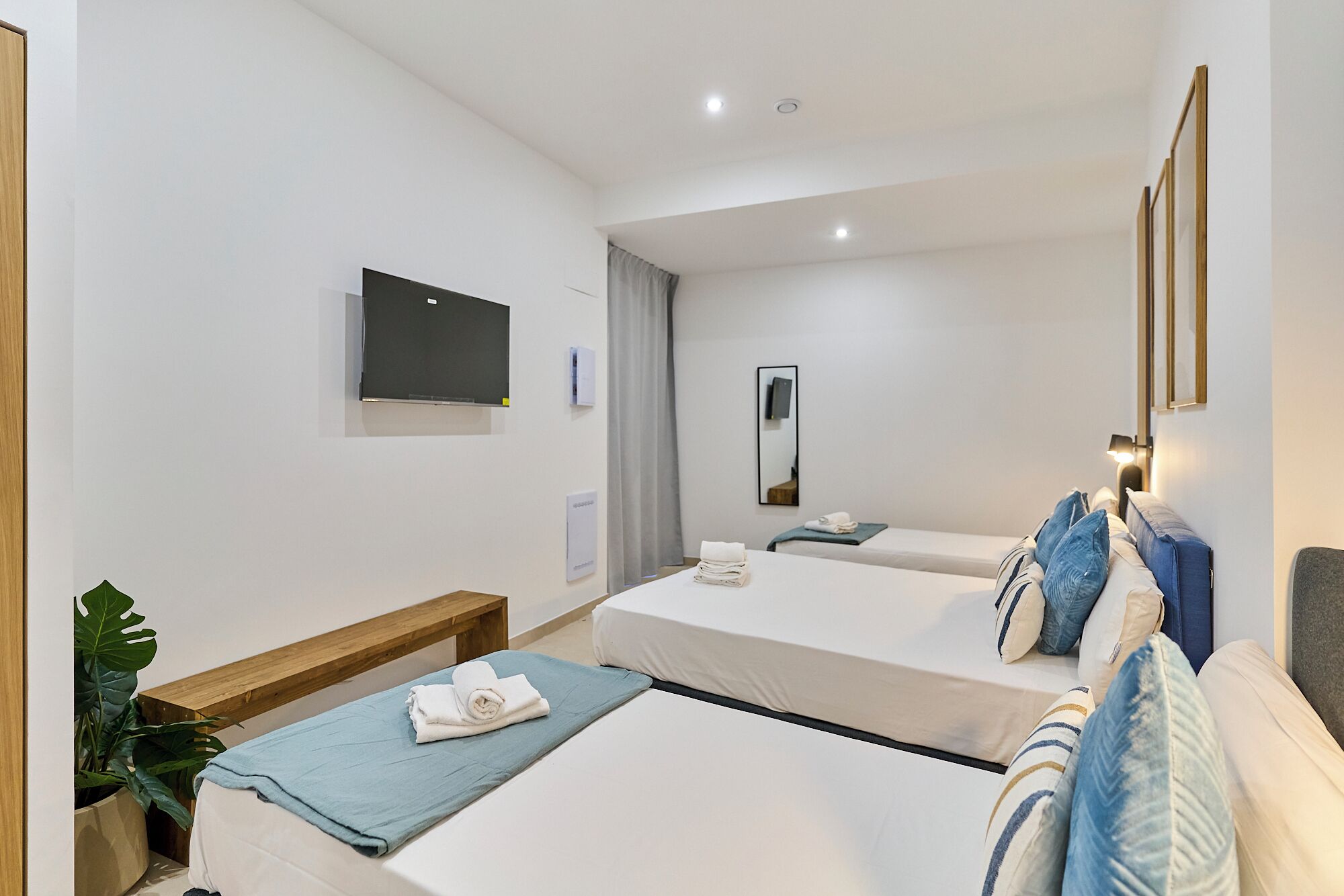 Habitación de hotel con dos camas, televisión, espejo y mesita de noche con lámpara.