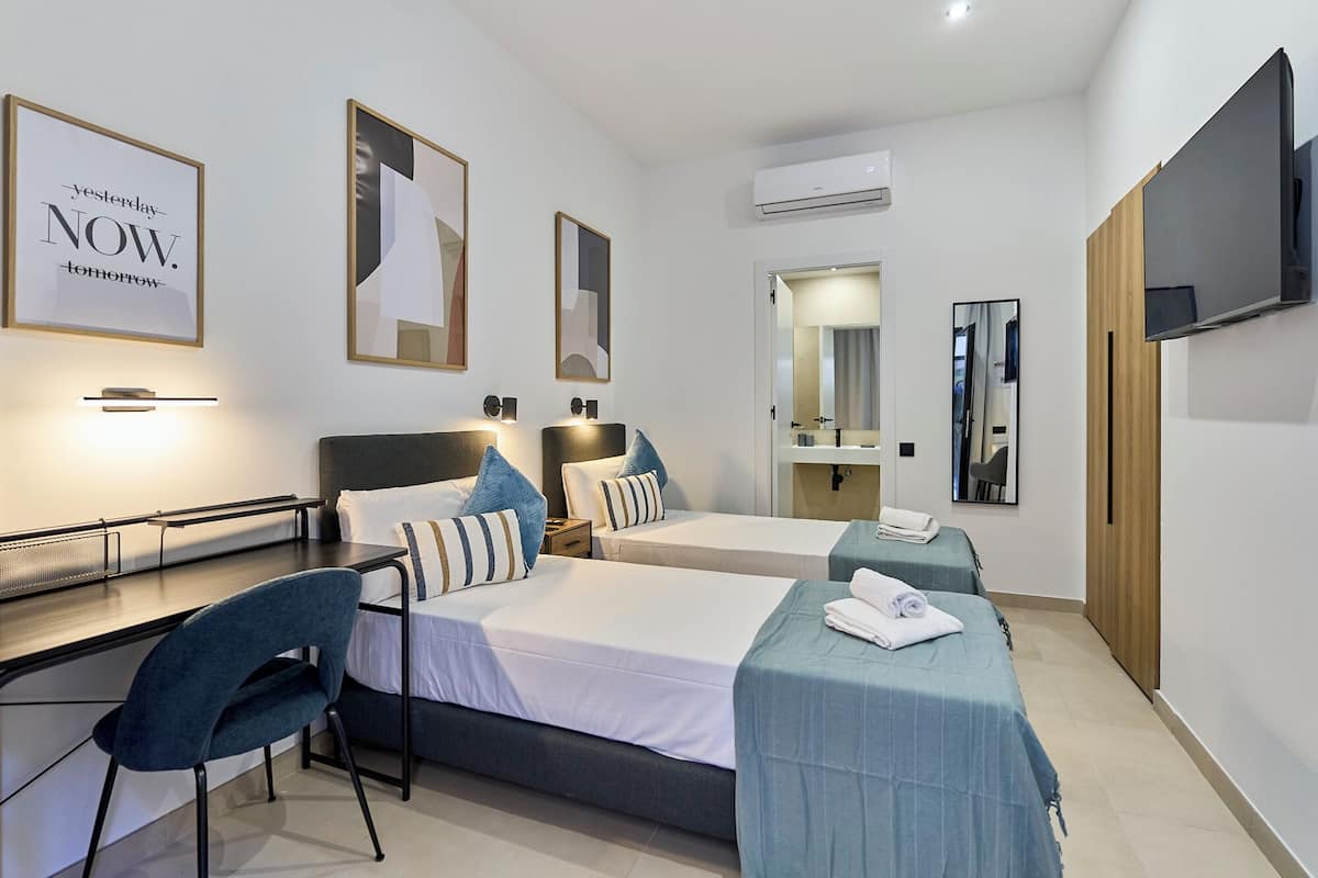 Une chambre d’hôtel avec deux lits, un bureau, une chaise, une télévision et un miroir.