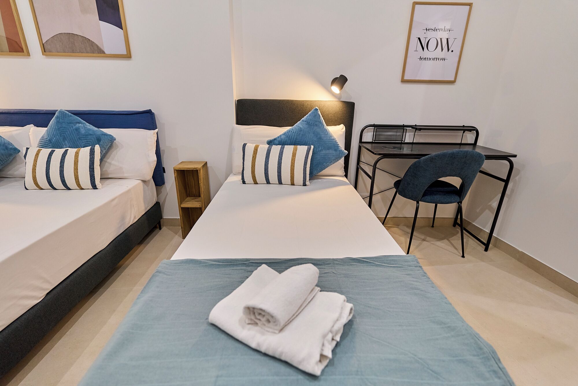Ein Hotelzimmer mit zwei Betten, einem Schreibtisch, einem Stuhl und einem kleinen Nachttisch.