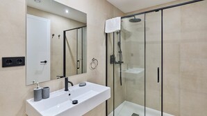 A modern bathroom with a glass-enclosed shower, a white sink with two soap dispensers, and a large mirror. - Sant Adrià Urban Suites by gaiarooms (Badalona)