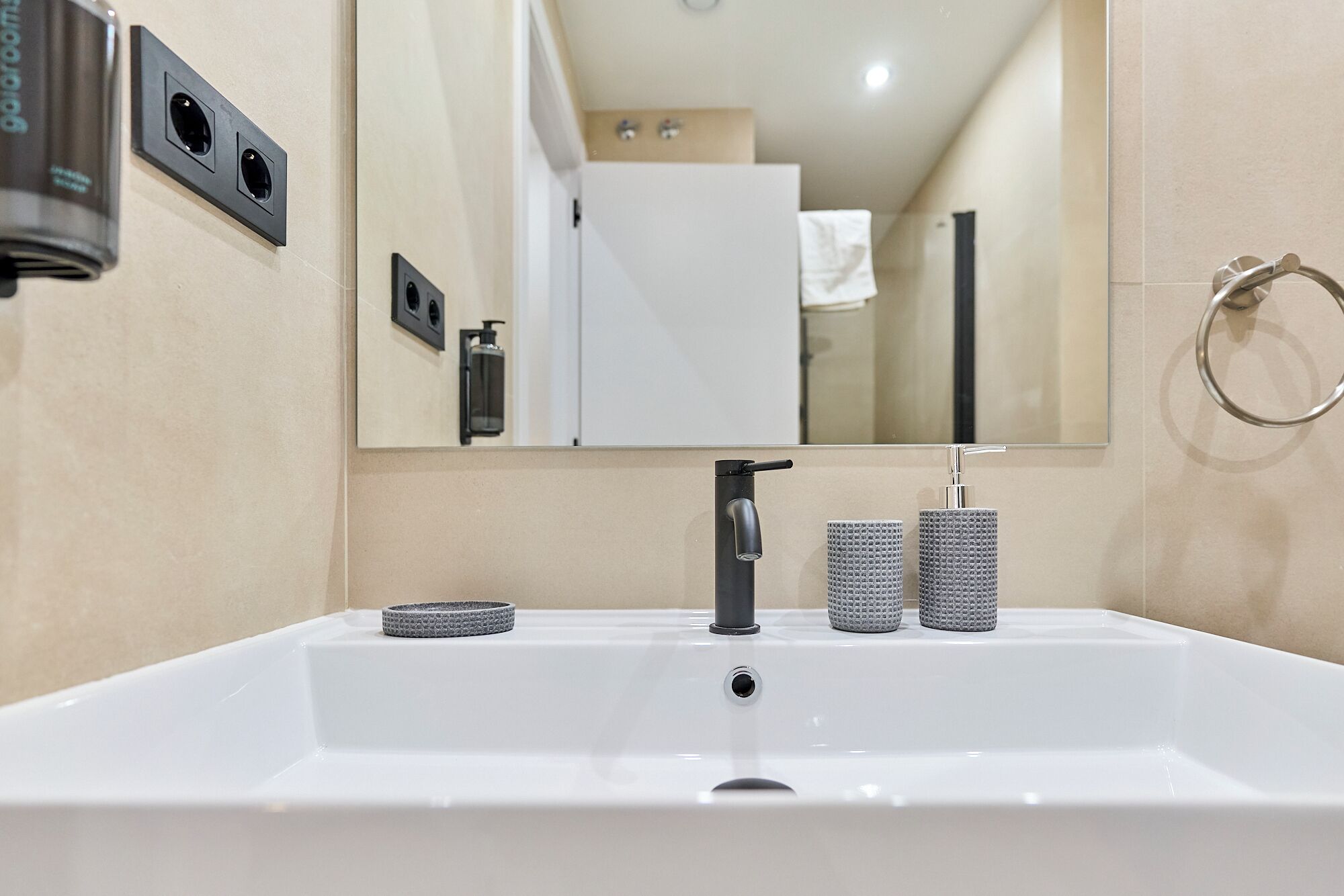 A modern bathroom with a white sink, a mirror, and two soap dispensers.