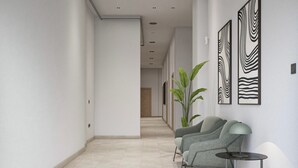 A modern hallway with a light-colored floor, a potted plant, and two grey armchairs with a small table and lamp. - Sant Adrià Urban Suites by gaiarooms (Badalona)