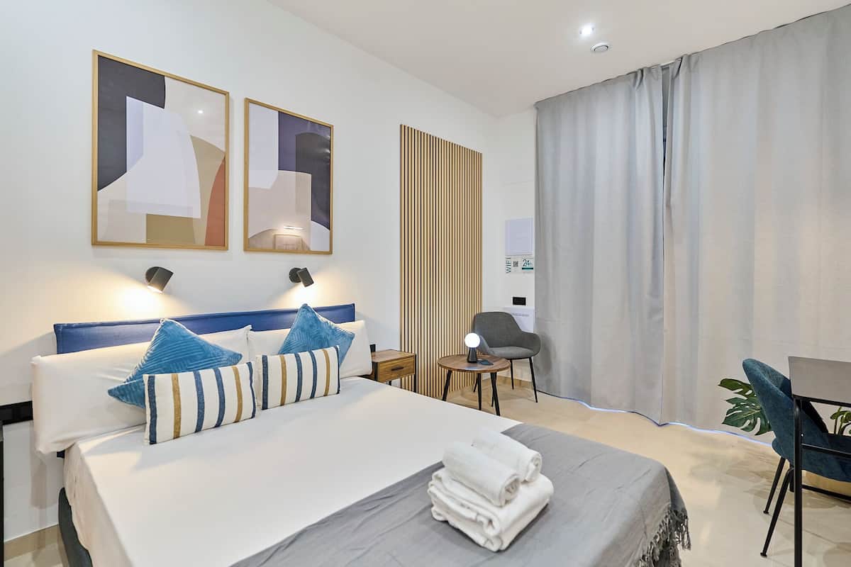 Une chambre d’hôtel moderne avec un lit bien fait, un bureau, une chaise et une grande fenêtre avec des rideaux.