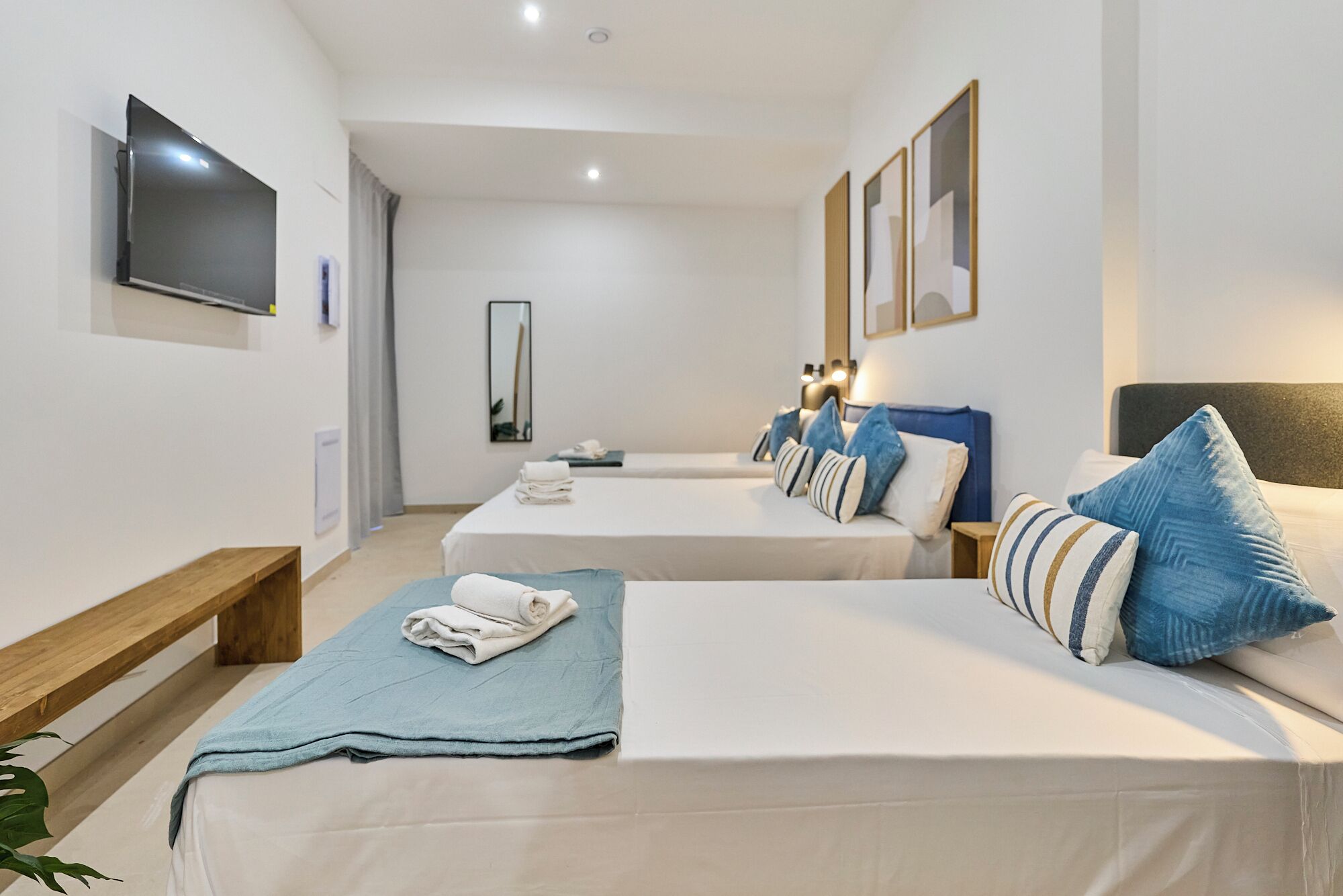 A hotel room with two beds, a TV, a mirror, and a bedside table with a lamp.