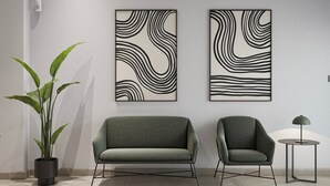 A modern interior with two abstract wall art pieces, a green sofa, a matching armchair, a small round table, and a potted plant. - Sant Adrià Urban Suites by gaiarooms (Badalona)