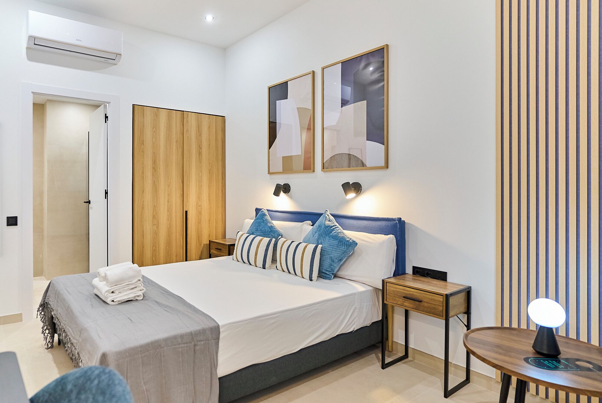 Un dormitorio moderno con cama, mesitas de noche, un escritorio y una lámpara.