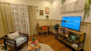 A cozy living room with a wooden sofa, a dining table, a TV, and a bookshelf. - Royal Spark Residency (Gurugram)