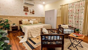 A cozy bedroom with a bed, two chairs, a small table, a wardrobe, and a potted plant. - Royal Spark Residency (Gurugram)