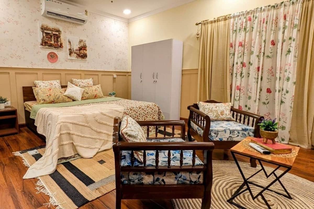 Een gezellig slaapkamer met een bed, twee stoelen, een klein tafeltje, een kast en een plant in pot.