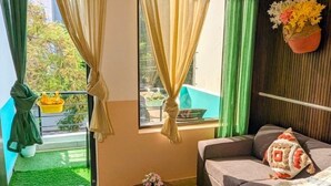 A cozy living room with a sofa, a small table, and a window with curtains. - Royal Spark Residency (Gurugram)
