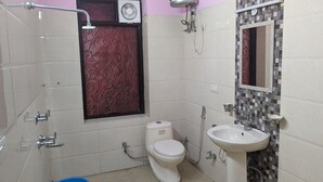 A small bathroom with a toilet, sink, shower, and decorative tiles. - Royal Spark Residency (Gurugram)