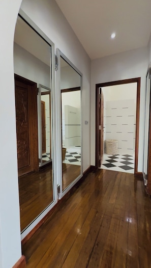 A hallway with wooden flooring, a mirrored closet door, and a checkered floor pattern in the background.