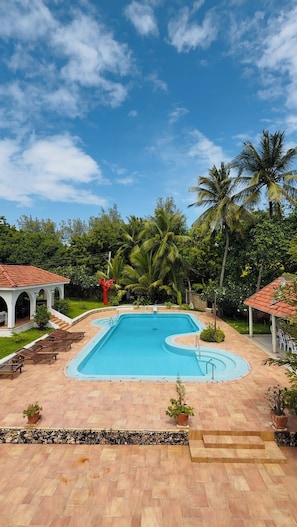 A swimming pool with a curved edge, surrounded by a tiled deck and lounge chairs.