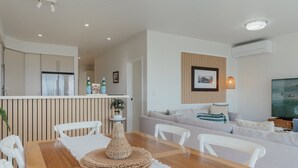 Una sala de estar moderna con una mesa de comedor de madera, sillas blancas, un sofá y una televisión.