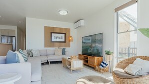 Una sala de estar moderna con un sofá, una televisión, un sillón de mimbre y un ventanal grande.