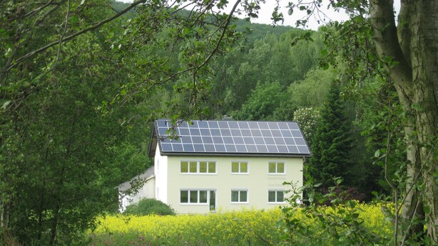 A house with solar panels, surrounded by lush greenery and a field of yellow flowers. - Ferienwohnung im Dachgeschoss, Homberg (Homberg)