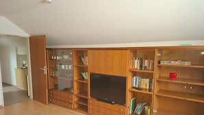 A spacious living area with wooden furniture, a television, and bookshelves. - Ferienwohnung im Dachgeschoss, Homberg (Homberg)