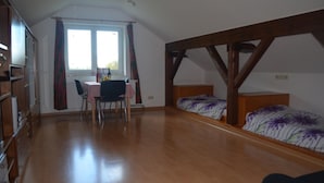 A room with a wooden floor, a bed with floral bedding, a desk with a chair, and a window with curtains. - Ferienwohnung im Dachgeschoss, Homberg (Homberg)