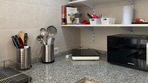Keittiössä on graniittitasot, ruostumattomasta teräksestä valmistetut keittiövälineet, Samsungin mikroaaltouuni ja keittokirja hyllyssä.