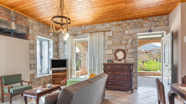 Un salon chaleureux avec un mur en pierre, un plafond en bois, une télévision, un canapé, une commode en bois et un coin repas.