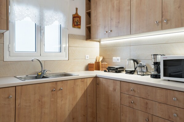 A kitchen with wooden cabinets, a white countertop, a sink, a window, and a microwave.