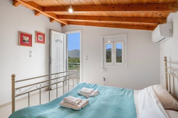 A bedroom with a bed, a window, a door, and a view of the outdoors.