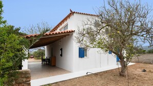 A white building with a tiled roof, a covered patio, and a tree with sparse foliage.