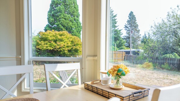 A dining area with a table, chairs, and a view of the backyard through large windows.