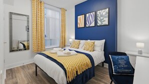 Una habitación de hotel con cama, una silla, un escritorio, un espejo y obras de arte en la pared.