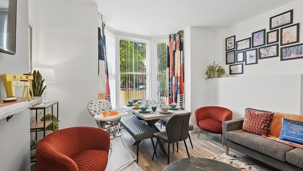 Una sala de estar moderna con comedor, que incluye un sofá, sillas, una mesa dispuesta para comer y un gran ventanal con cortinas.