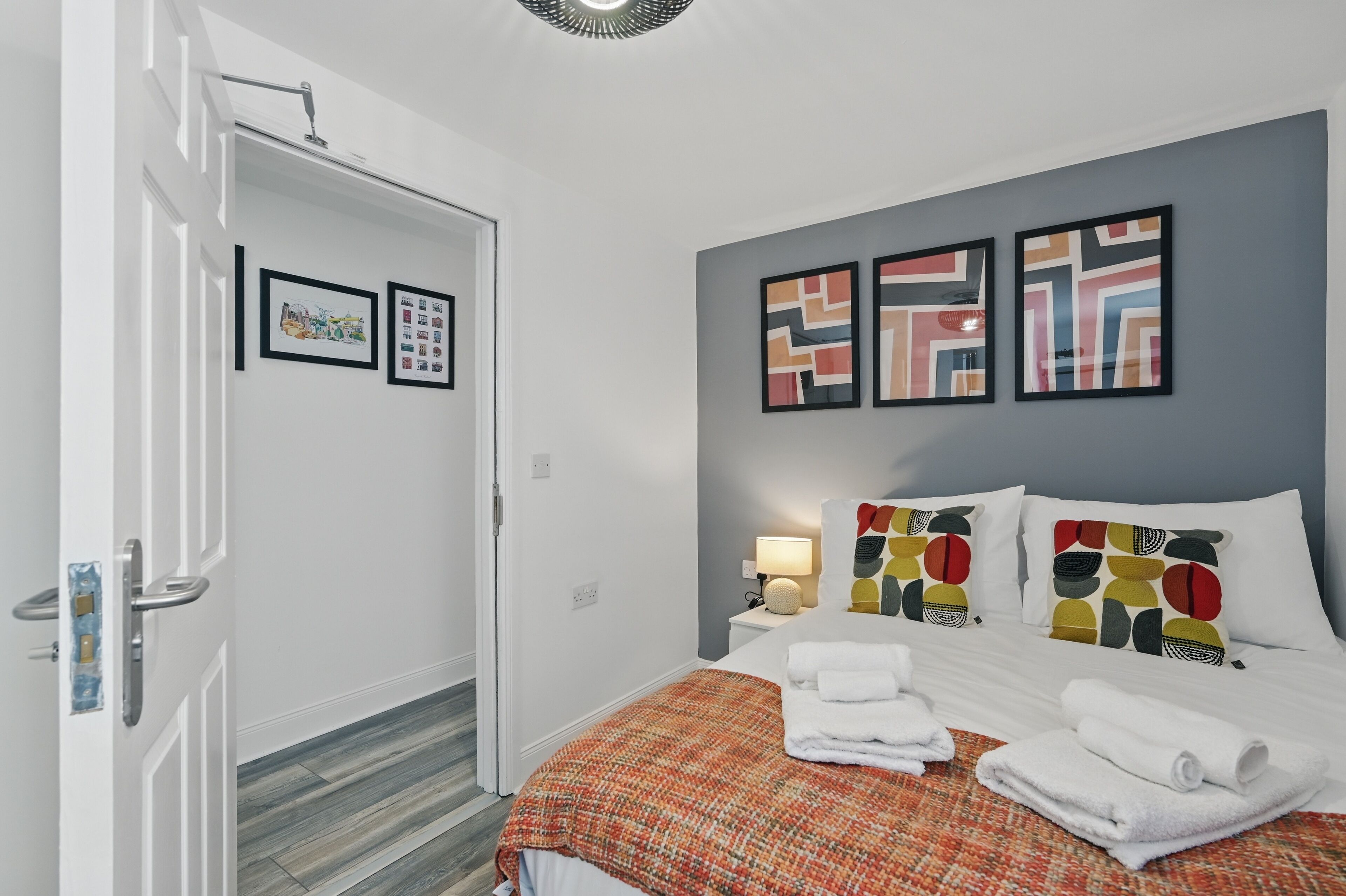 A hotel room with a bed, pillows, a nightstand, a lamp, and artwork on the wall.