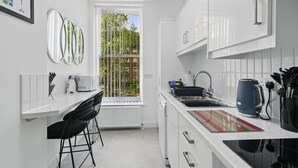 Una cocina moderna con armarios blancos, encimera negra, ventana con vistas a árboles y una cafetera.